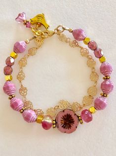 a bracelet with pink beads and gold accents on it's end is sitting on a white surface