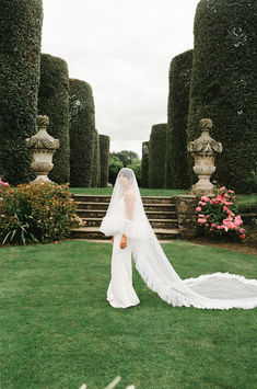 a woman in a wedding dress is standing on the grass with her veil over her head