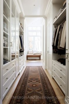 a large white closet with lots of drawers and clothes hanging on the walls, along with a rug