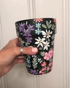 a hand holding up a black floral cup with pink, white and blue flowers on it