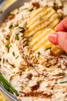 a hand dipping crackers into a bowl of dip