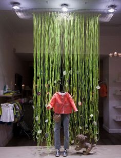 a mannequin standing in front of a display of green plants