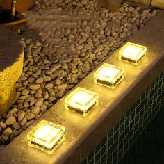 some lights are lit up on the side of a wall with rocks and stones around it