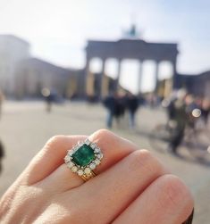 a close up of a person's hand holding a ring with an emerald and diamond center