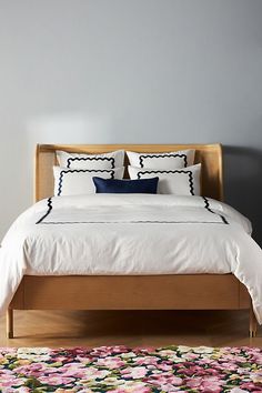 a bed with white sheets and pillows on top of it next to a colorful rug