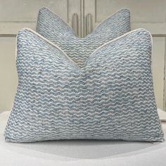 two blue and white pillows sitting on top of a bed