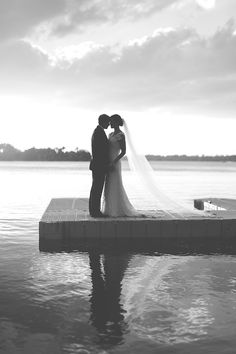 a bride and groom standing on a dock by the water