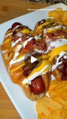 two hot dogs covered in cheese and toppings on a plate with potato chips next to it