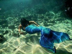 a woman is swimming in the water with a blue fish on her back and long hair