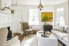 a living room with white furniture and yellow flowers in vases on the fireplace mantel