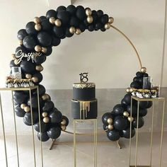 a black and gold balloon arch with a cake on the table in front of it