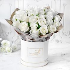 a bouquet of white roses in a round box on a marble countertop next to flowers