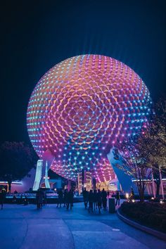 people are walking around in front of a large ball at night with lights on it