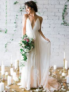 a woman standing in front of a white brick wall with flowers and greenery on it