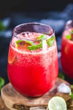 two glasses filled with red liquid and garnished with mint on a wooden board