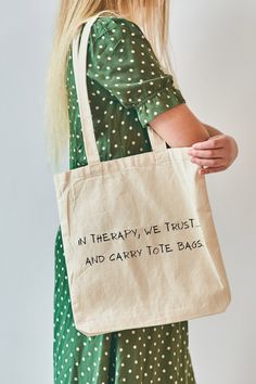 a woman carrying a tote bag that says in therapy we trust and carry tote bags