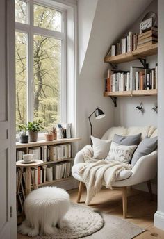 a white chair sitting in front of a window next to a book shelf filled with books