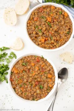 two bowls filled with beans and carrots on top of a white table next to bread