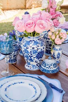 a table set with blue and white china, pink roses in vases and plates