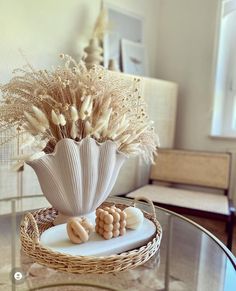 a glass table topped with a vase filled with dried flowers and seashells on top of it