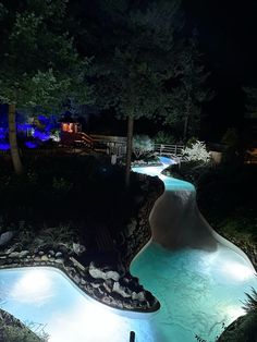 an outdoor swimming pool lit up at night with lights in the water and trees around it