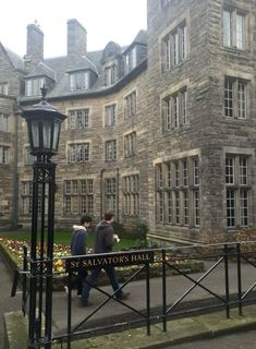 two people walking down the sidewalk in front of an old building