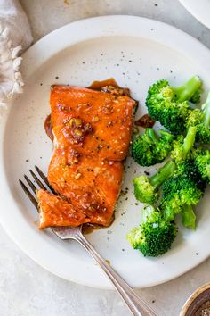 a piece of salmon and broccoli on a plate with a fork next to it