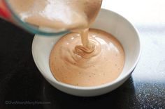 a person pouring sauce into a white bowl