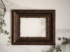 an old wooden frame sitting on top of a white wall next to eucalyptus branches and flowers