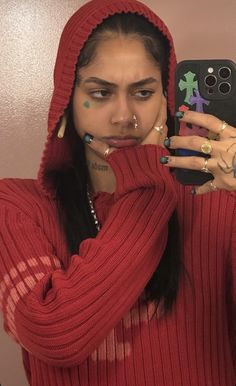 a woman with piercings taking a selfie in front of a mirror wearing a red sweater