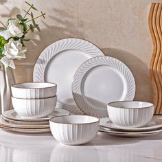 a white dinner set with gold trimmings sits on a table next to flowers