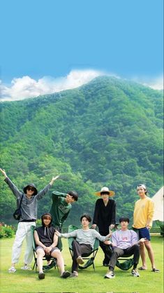 a group of people standing on top of a lush green field next to a mountain