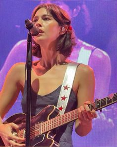 a woman holding a guitar and singing into a microphone