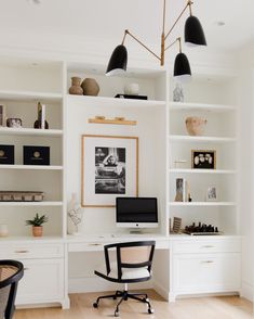 a home office with white bookcases, black chairs and a computer on the desk