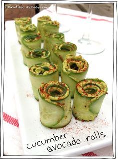 cucumber rolls are arranged on a white platter with wine glasses in the background