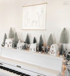 a white piano sitting in front of a wall with christmas trees and houses on it