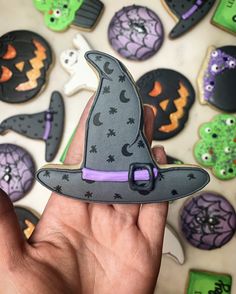 a hand holding a cookie shaped like a witch's hat with other decorated cookies behind it