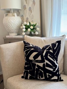 a black and white pillow sitting on top of a chair next to a vase with flowers