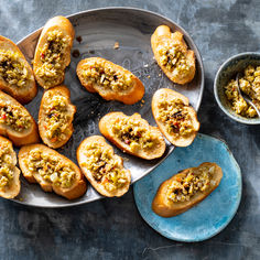 several pieces of bread with various toppings on a plate next to a small bowl