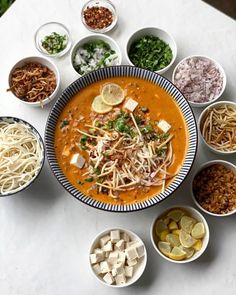 several bowls of food are arranged on a table with plates and bowls in the middle