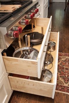 an open drawer in a kitchen with pots and pans on the bottom shelf,