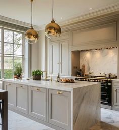 a large kitchen with marble counter tops and gold pendant lights hanging from the ceiling over the island