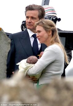 a man in a suit and tie holding a baby next to a woman wearing a white dress