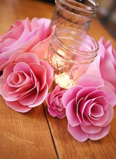 some pink flowers are sitting on a wooden table next to a jar with water in it