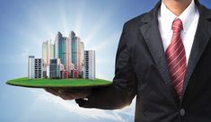 a man in a suit holding a green plate with buildings on it and the sky behind him