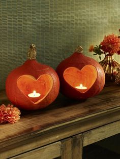 two carved pumpkins sitting next to each other on a wooden table with candles in the shape of hearts