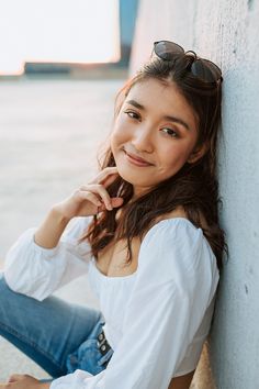 a woman leaning against a wall with her hand on her chin and looking at the camera