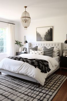 a bedroom with white and black bedding, chandelier, rugs and pictures on the wall