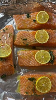 four pieces of salmon with lemons and herbs on them sitting on aluminum foil, ready to be cooked