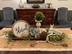 a wooden table topped with a vase filled with flowers and greenery next to a sign that says blessed